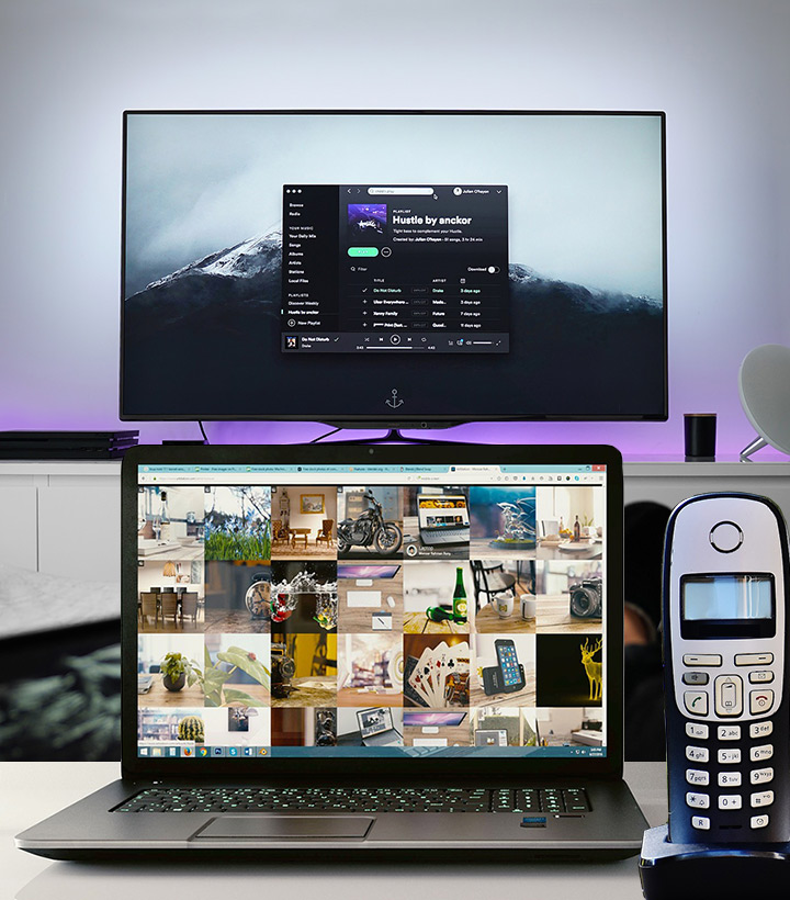 laptop computer and land line phone in foreground with television in the background